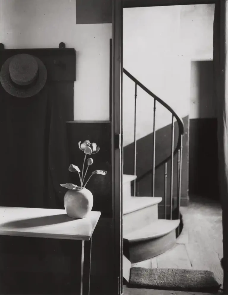 André Kertész Art Photography poster featuring a black and white image of a vase on a table next to a doorway revealing a winding spiral staircase.