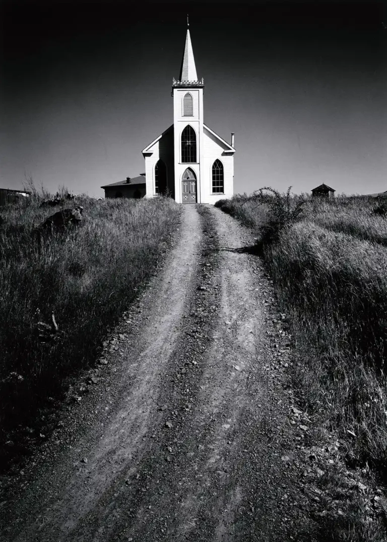 Ansel Adams Art poster featuring a dramatic black and white photograph of an isolated white church atop a grassy hill, viewed via a gravel path.