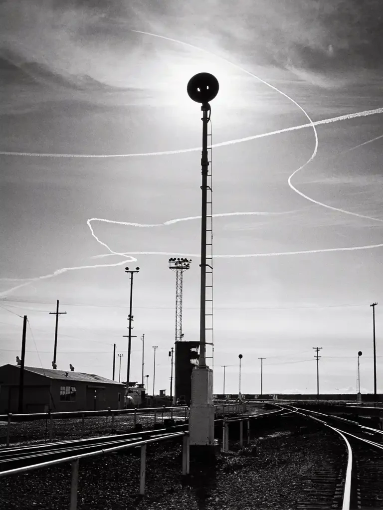 Ansel Adams photography poster featuring a tall railroad signal silhouetted against a dramatic sky with curving jet contrails in high-contrast black and white.