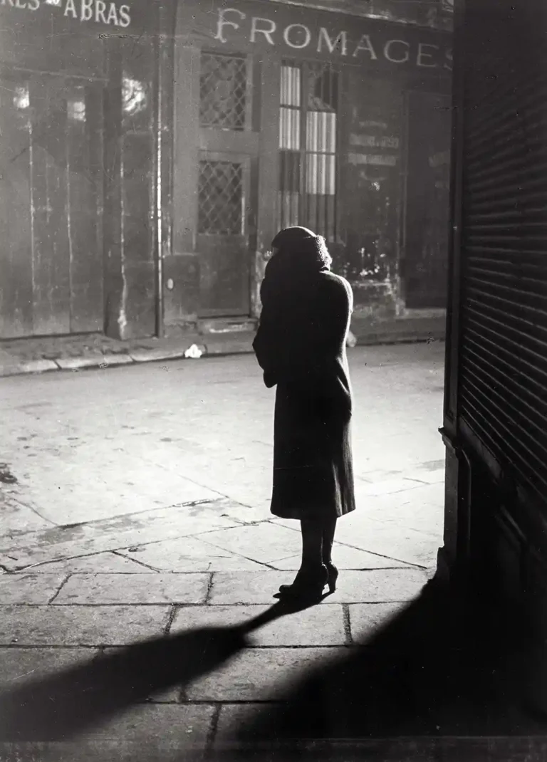 Brassaï black and white Art Photography poster featuring a solitary woman silhouetted on a Paris street at night, casting a long shadow.