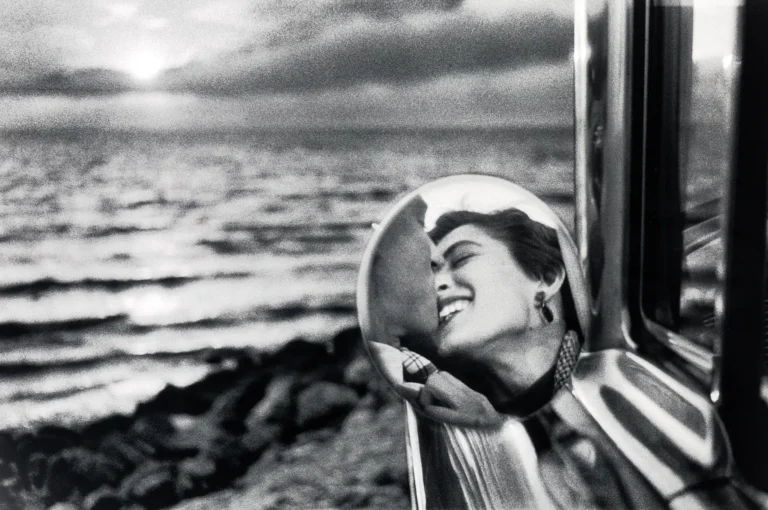 Elliott Erwitt fine art photography poster featuring a smiling woman's reflection in a side mirror, set against a dark ocean landscape backdrop.