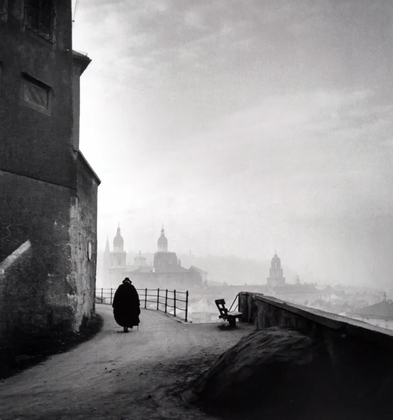 Ernst Haas black and white fine art photography poster featuring a solitary monk walking on a foggy street overlooking Salzburg, Austria.