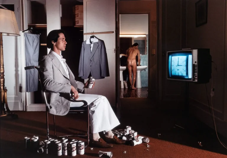 Guy Bourdin Fine Art photography poster featuring a man sitting amongst beer cans while a nude figure stands in the background doorway.
