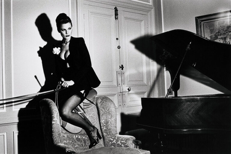 Helmut Newton fine art photography poster featuring a model sitting on a luxurious chair holding reins in a dramatic black and white interior with a piano.