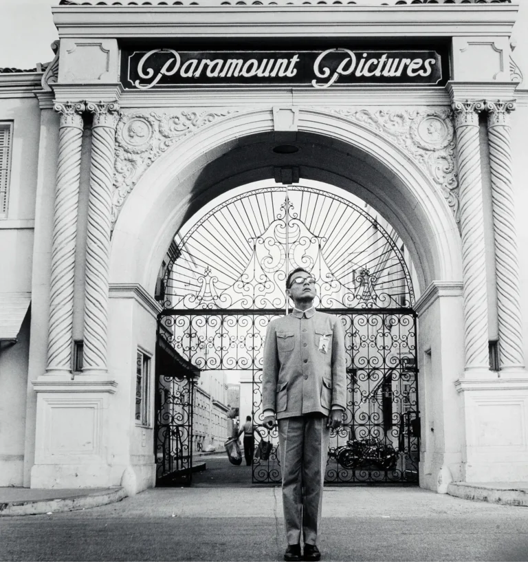 Kwong Chi Tseng conceptual art photography poster featuring the artist in a Mao suit standing before the ornate gates of the Paramount Pictures studio.