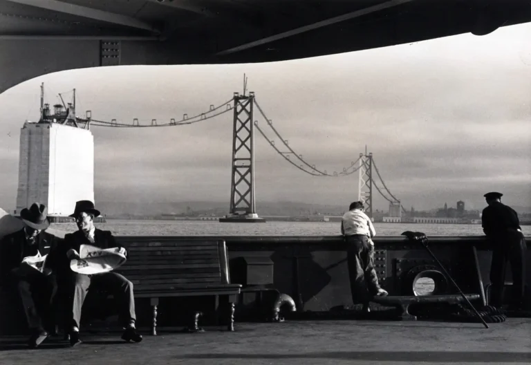 Peter Stackpole historic photography poster featuring men on a ferry deck viewing the massive San Francisco Bay Bridge during its construction in black and white.