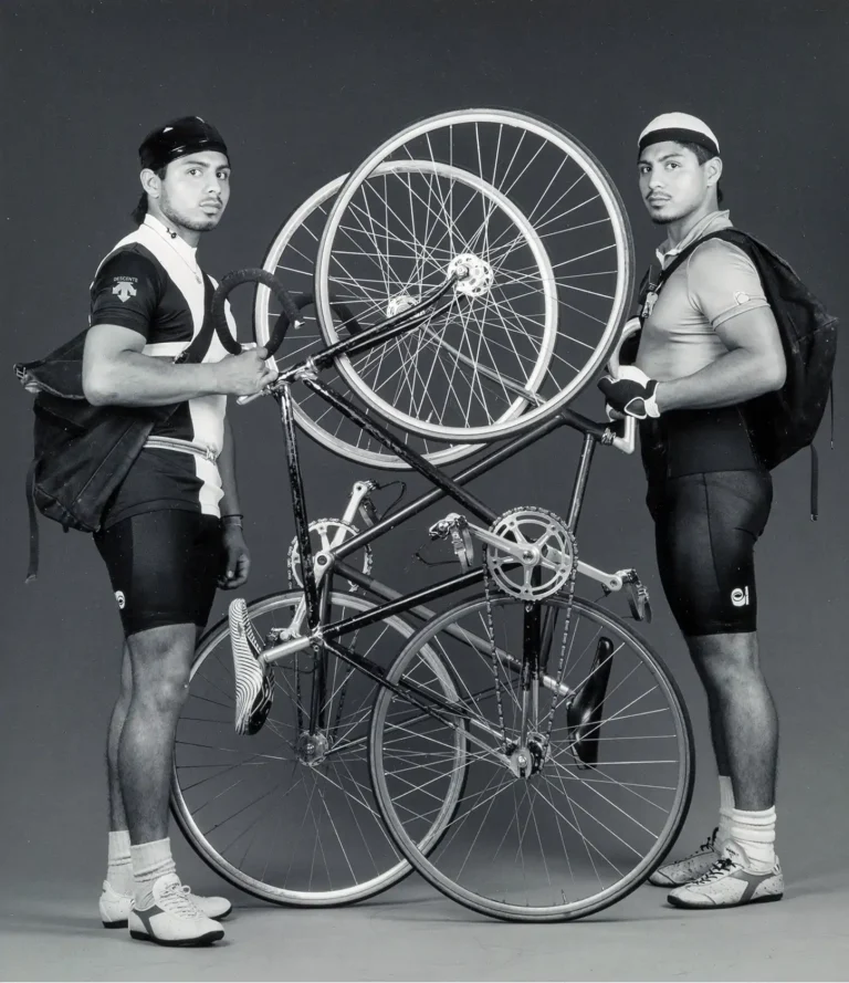 Robert Mapplethorpe Fine Art Photography poster featuring two male cyclists posing formally with overlapping bicycles against a grey background.