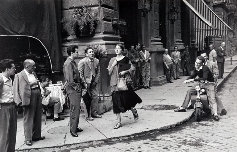 An American Girl in Italy Art poster by Ruth Orkin, featuring Ninalee Craig walking through a crowd of staring men in Florence, Italy, 1951.