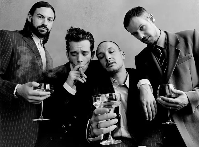 The 1975 Music poster featuring the band members in suits, holding drinks, in a stylish black and white photograph.
