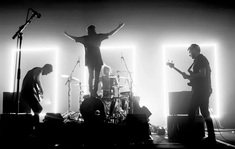 The 1975 Music poster featuring Matty Healy silhouetted on stage with arms outstretched, surrounded by bandmates and bright rectangular lights in black and white.