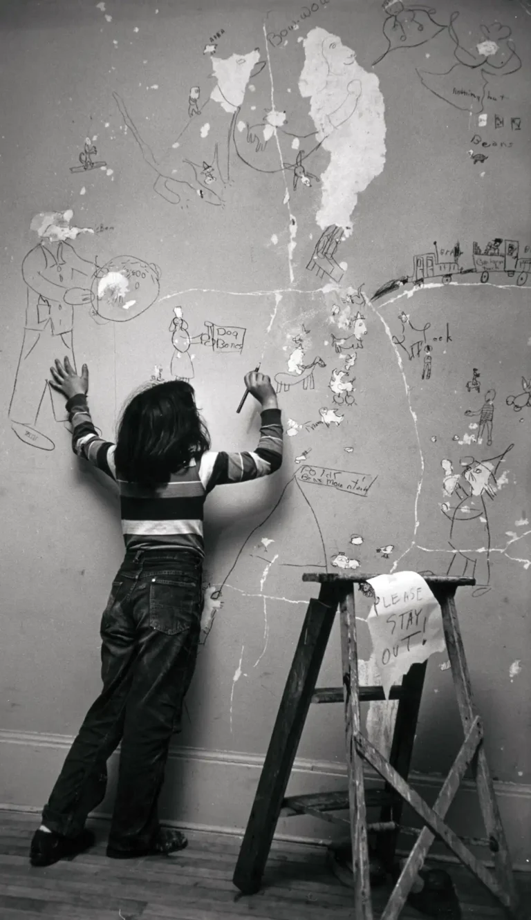 Nostalgic photography poster featuring a child with their back to the viewer, drawing on a distressed wall covered in whimsical sketches and peeling paint.