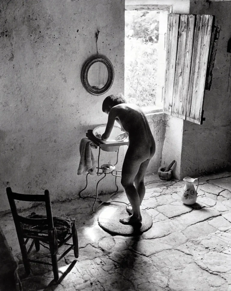 Willy Ronis 'Le Nu Provençal' black and white photography poster featuring a nude figure washing at a basin in a rustic, sunlit French room.
