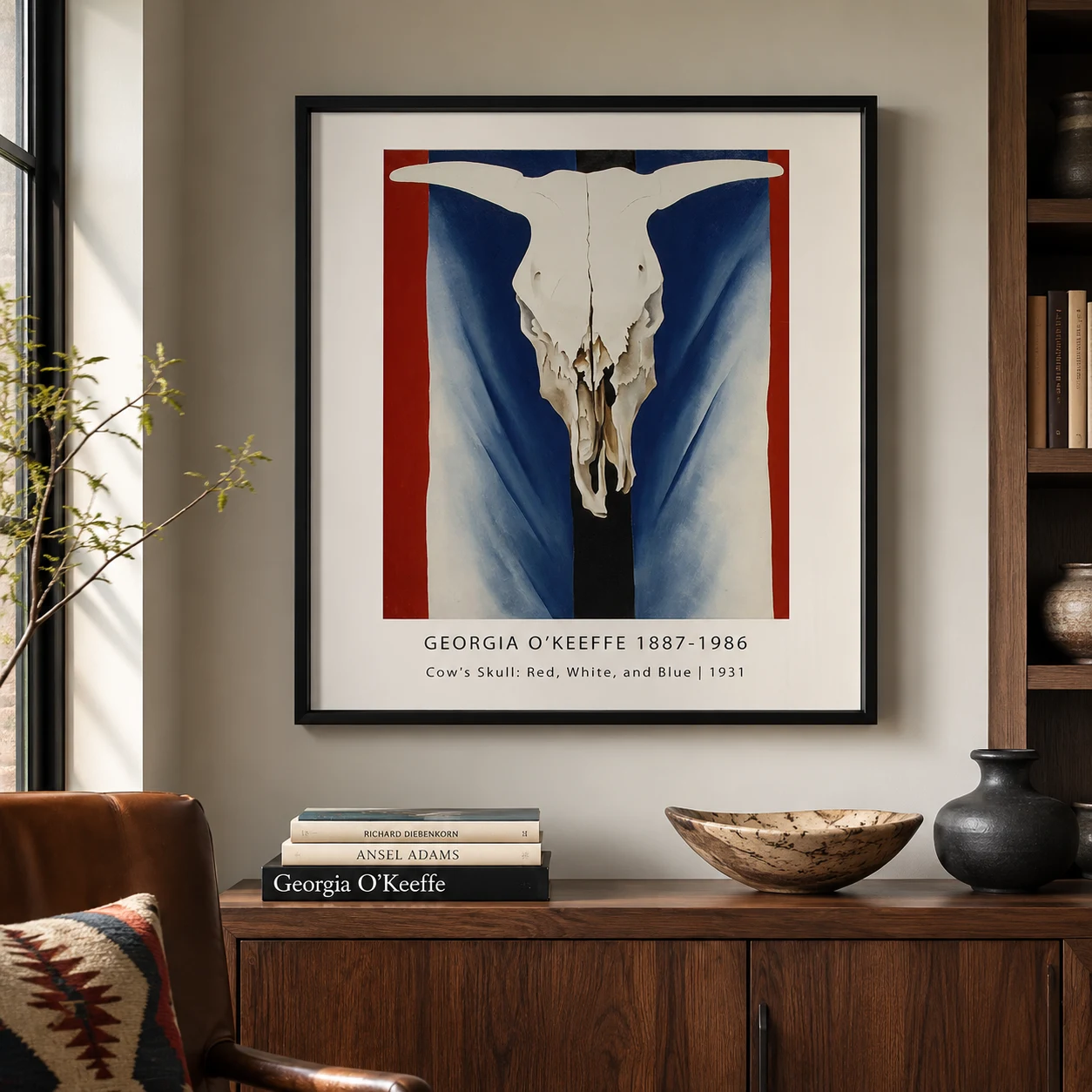 Room mockup of Cow Skull Print, Red White Blue Georgia O'Keeffe Wall Art Print, displayed as framed wall art in a living room setting as a portrait print with blue, red, and black tones.