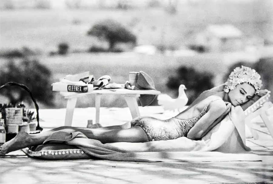 Audrey Hepburn wearing a floral swim cap and swimsuit lounging on a sunbed in a monochrome Two for the Road film still.