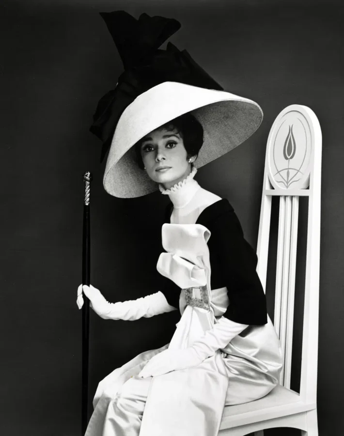 Audrey Hepburn as Eliza Doolittle in a black and white fashion portrait wearing a large hat and white gloves.