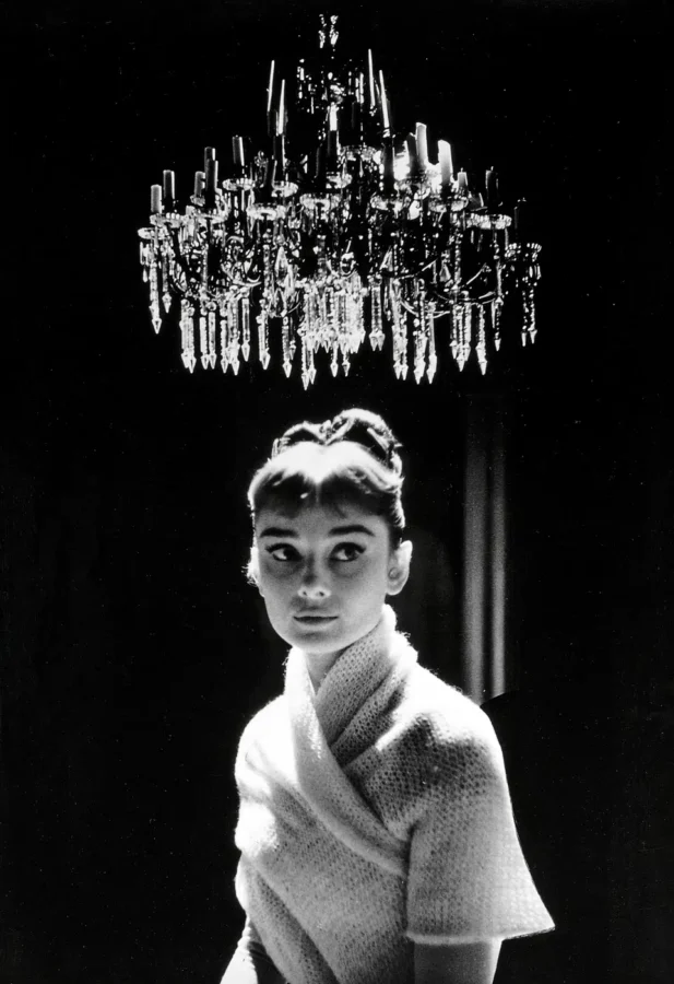 Audrey Hepburn as Natasha Rostova in War and Peace under a crystal chandelier in black and white photography.
