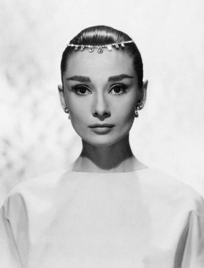 A black and white portrait of Audrey Hepburn from 1956 wearing a thin jeweled tiara and looking directly at the camera.