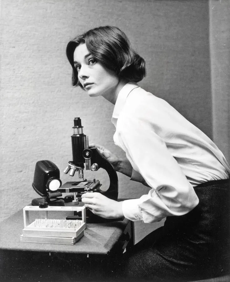 Black and white photograph of Audrey Hepburn as Sister Luke using a microscope in the film The Nun's Story.