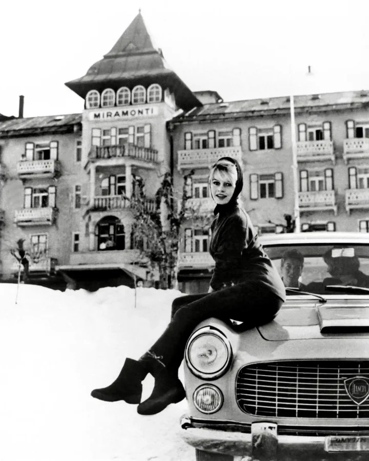 Brigitte Bardot in 1959 sitting on a Lancia car hood in the snow in front of the Miramonti Hotel in Cortina, Italy.