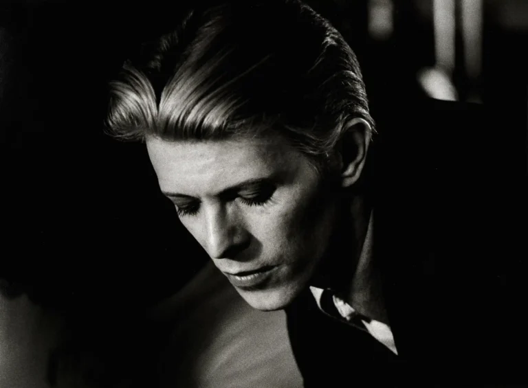 Clean artwork view of David Bowie in Los Angeles Restaurant Monochrome Photography Print. A quiet black and white photograph of David Bowie looking down in a Los Angeles restaurant, featuring high-contrast lighting and a sophisticated mood.