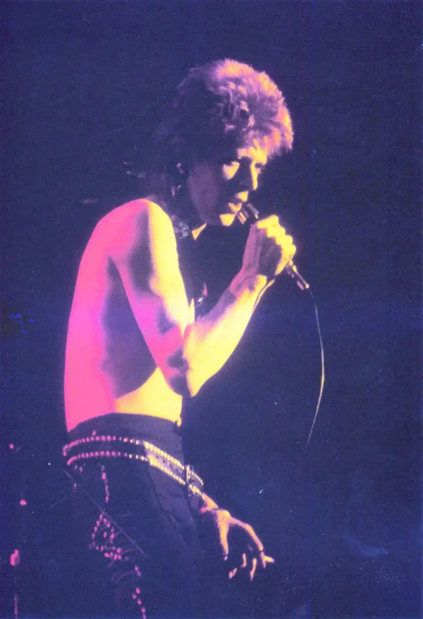 David Bowie Moonage Daydream — grainy, high-contrast concert photograph of David Bowie performing as