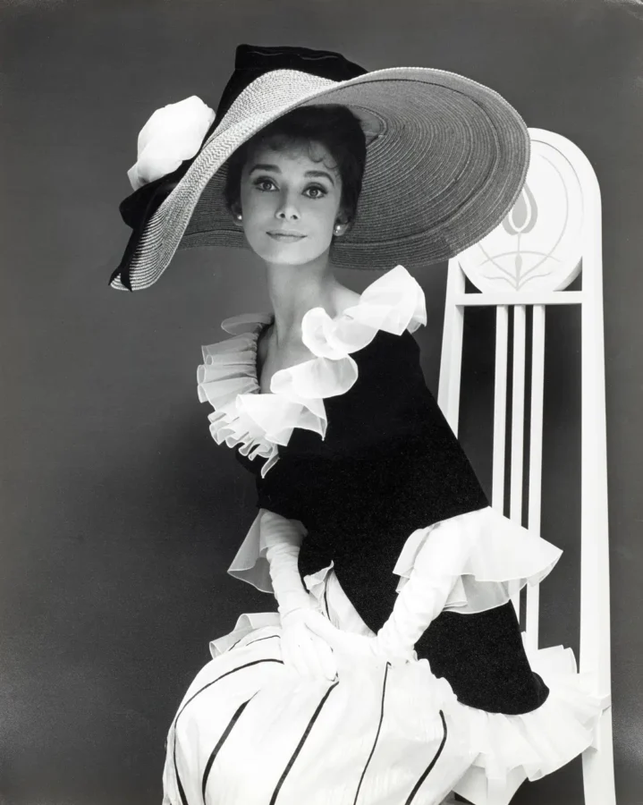 Audrey Hepburn in the Ascot dress from My Fair Lady featuring a large hat and ruffled collar in black and white photography.
