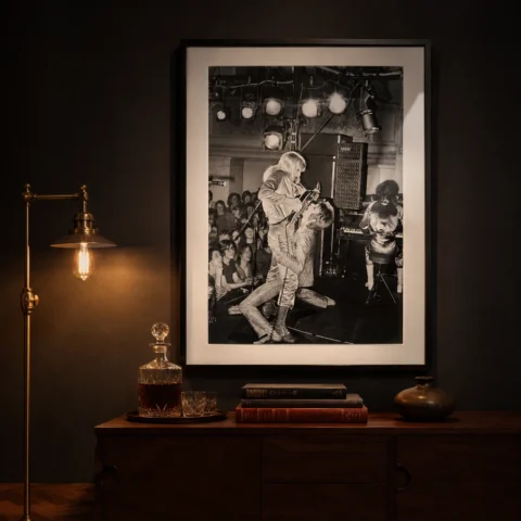 A framed black and white David Bowie concert print hanging above a minimalist wooden sideboard in a modern living room.