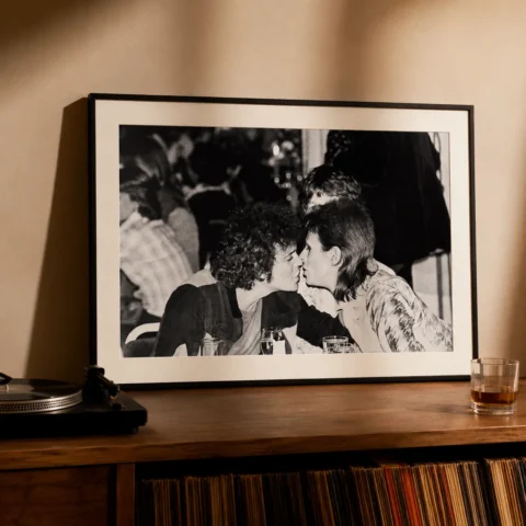 A framed David Bowie and Lou Reed art print hanging on a clean gallery wall above a record player setup.