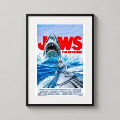 A vertical framed jaws the revenge art print hanging on a clean office wall above a dark wooden desk.