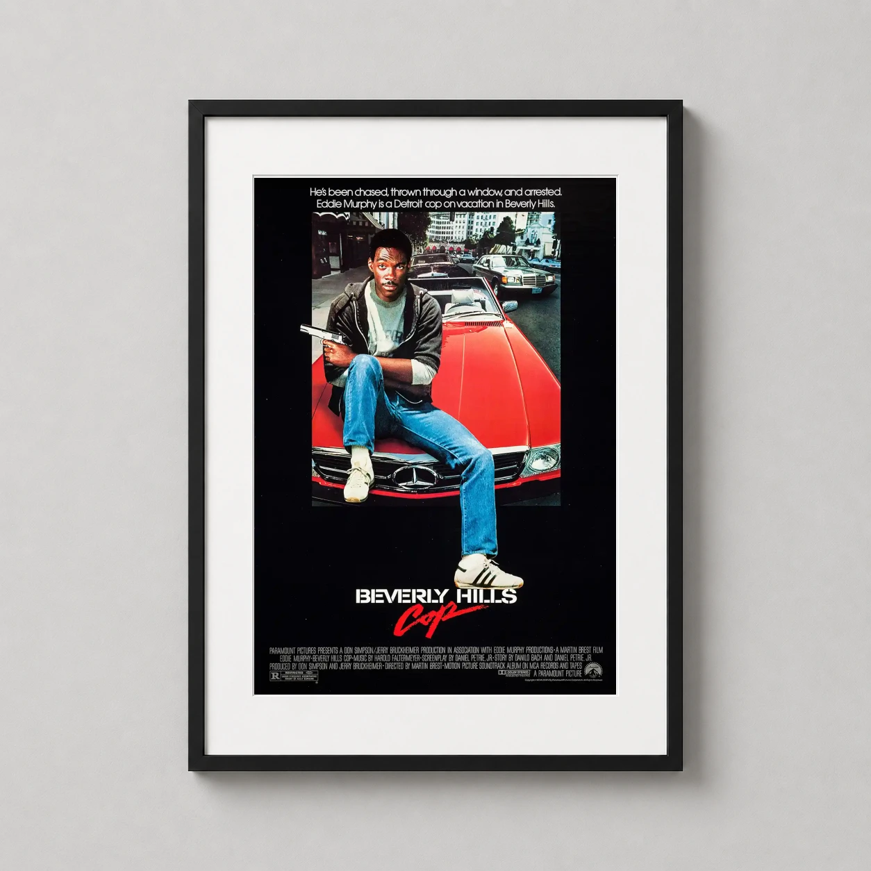 Room mockup of Axel Foley Beverly Hills Cop 1984 Vintage Action Movie Poster, displayed as framed wall art in a home theater setting as a portrait print with red tones.
