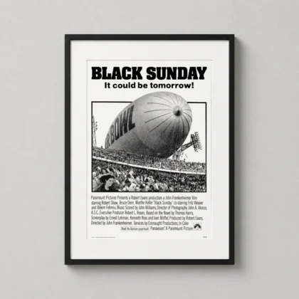A framed Black Sunday movie art print depicting a blimp over the Super Bowl hangs on a modern gallery wall.