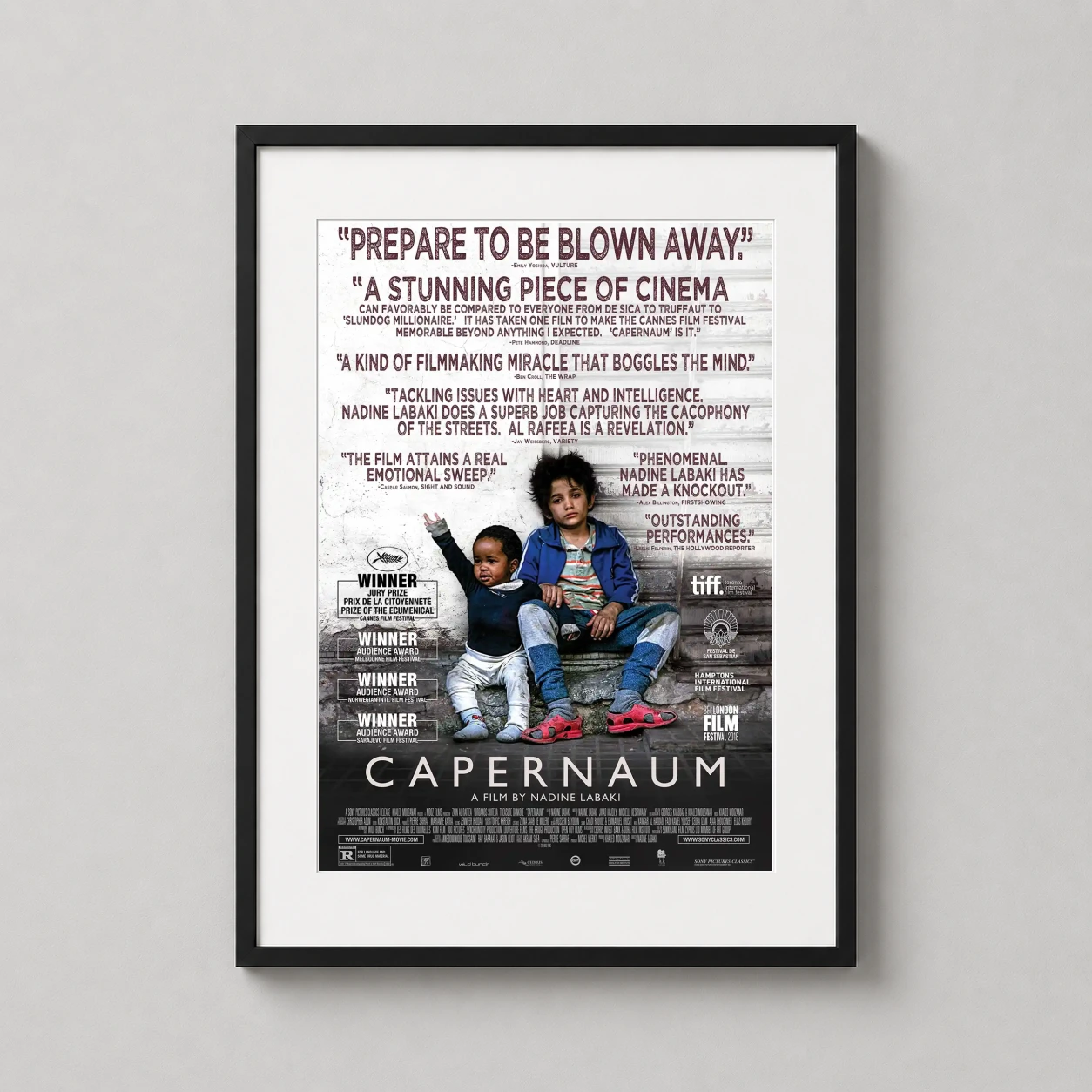 Room mockup of Capernaum Nadine Labaki Lebanese Drama Film Poster, displayed as framed wall art in a home theater setting as a portrait print with red tones.