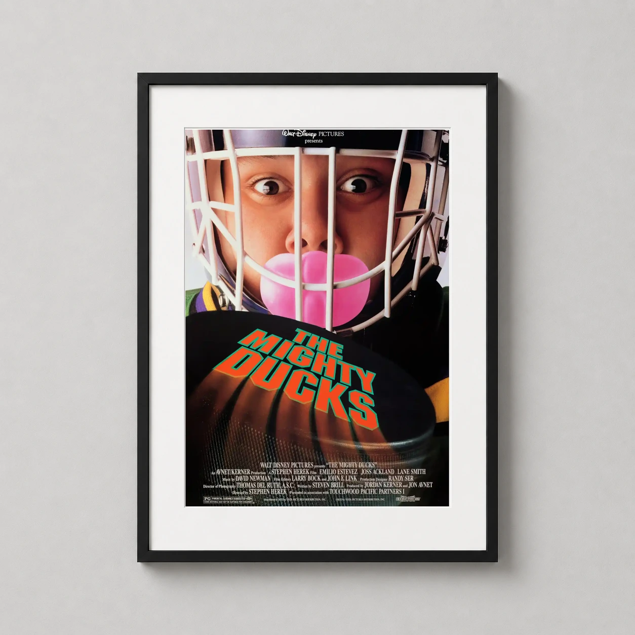 Room mockup of The Mighty Ducks 1992 Movie Retro Hockey Team Sports Movie Poster, displayed as framed wall art in a home theater setting as a portrait print with orange, pink, and black tones.