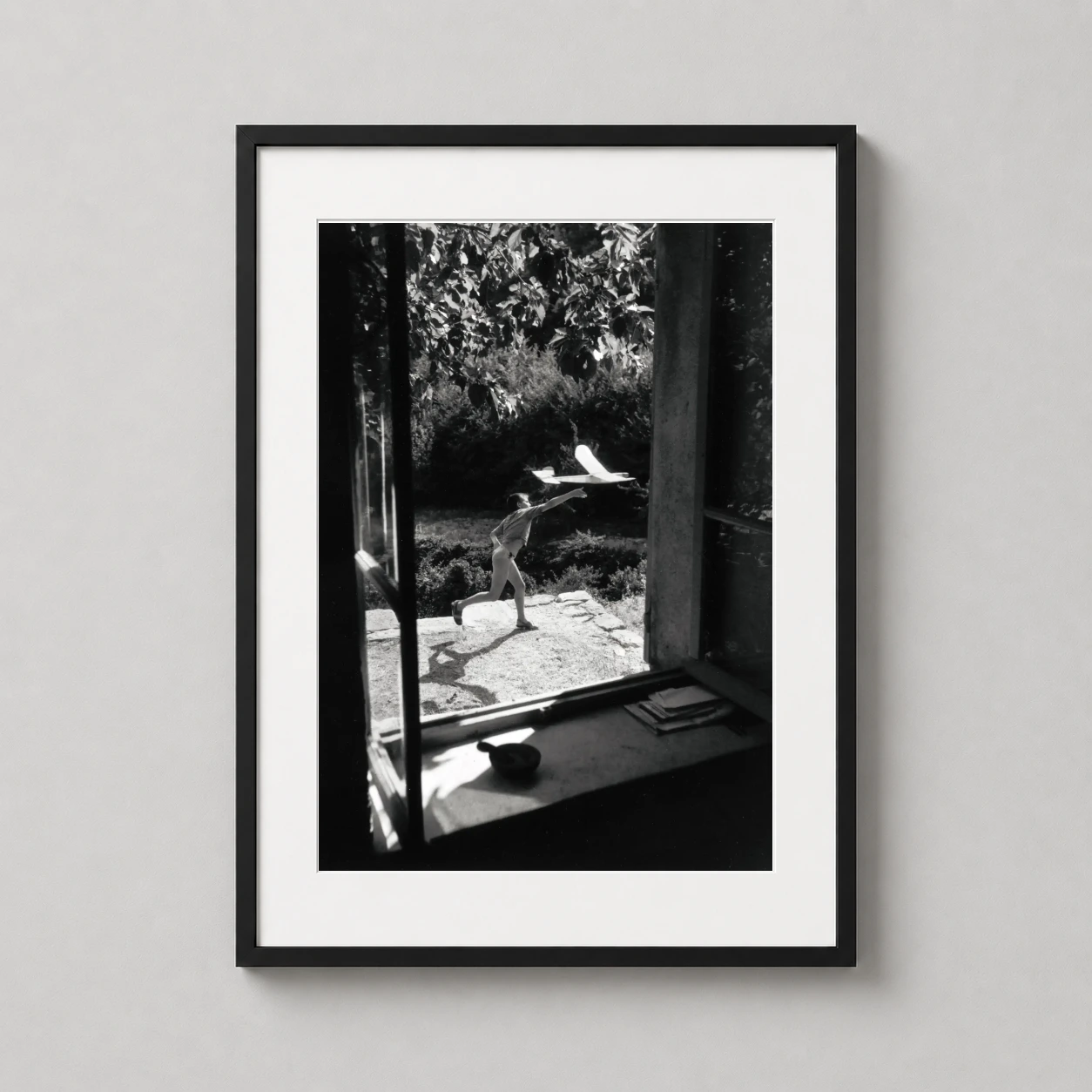 Room mockup of Willy Ronis Vincent Aeromodeliste Gordes 1949 Photography Print, displayed as framed wall art in a office setting as a portrait print with black and white tones.