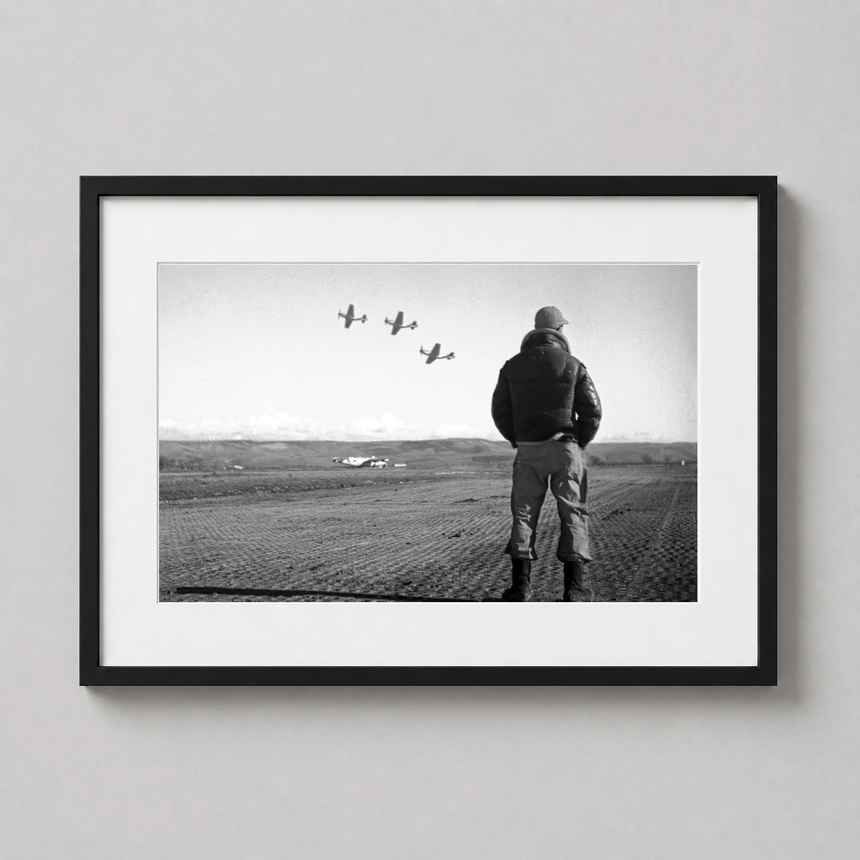 Room mockup of WWII Air Force Pilot Watching Airfield 1945 Photography Print, displayed as framed wall art in a office setting as a landscape print with black and white tones.