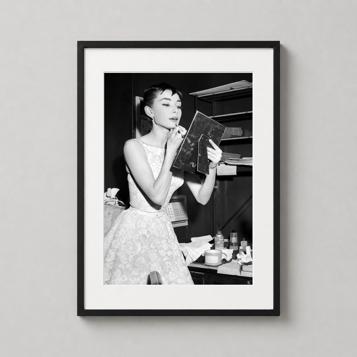 Room mockup of Audrey Hepburn Backstage Makeup Vintage Photography Print, displayed as framed wall art in a office setting as a portrait print with black and white and red tones.