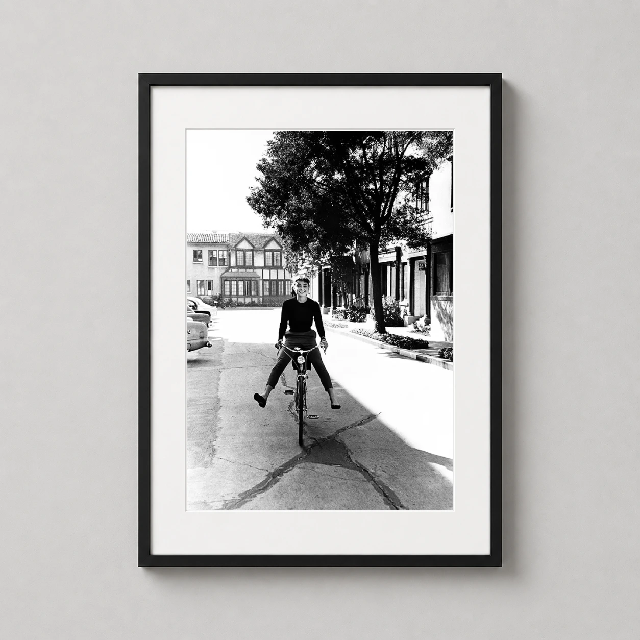 Room mockup of Audrey Hepburn on Bicycle Black and White Photography Print, displayed as framed wall art in a office setting as a portrait print with black and white and red tones.