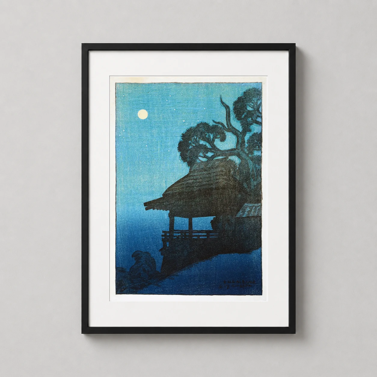 Room mockup of Ishiyama Temple Moonlight Kawase Hasui Japanese Woodblock Art Print, displayed as framed wall art in a bedroom setting as a portrait print with blue tones.