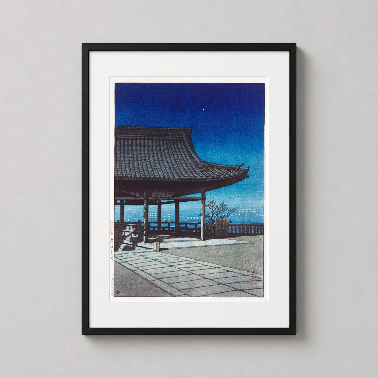 Room mockup of Kozu, Osaka, Kawase Hasui Japanese Woodblock Night Scene Art Print, displayed as framed wall art in a bedroom setting as a portrait print with blue tones.