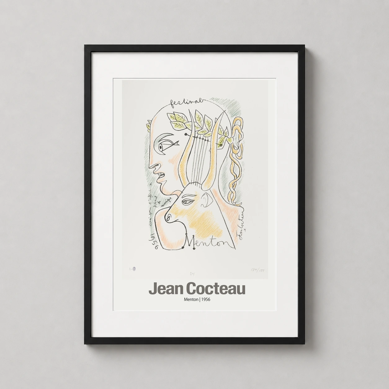 Room mockup of Jean Cocteau Menton 1956 Exhibition Art Print, French Riviera Poster, displayed as framed wall art in a living room setting as a portrait print with green, yellow, and pink tones.