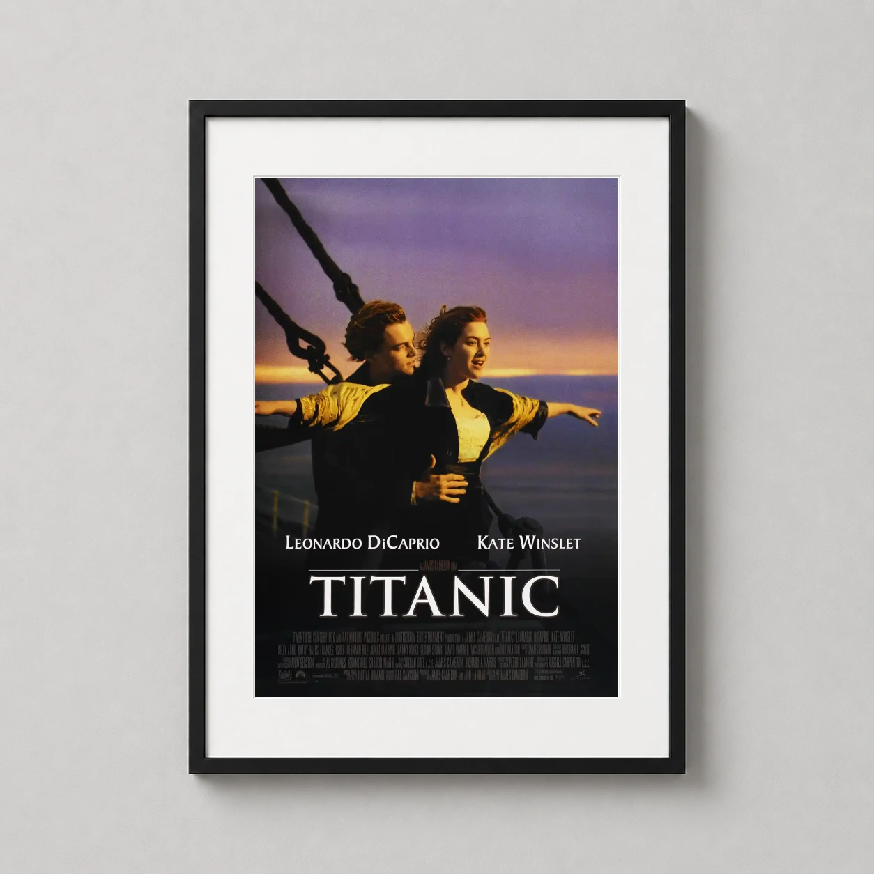 Room mockup of Titanic 1997 Movie Jack and Rose Bow Scene Movie Poster, displayed as framed wall art in a home theater setting as a portrait print with gold and pink tones.