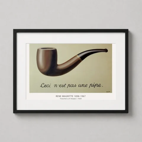 A framed Treachery of Images art print by René Magritte hanging in a modern home office.