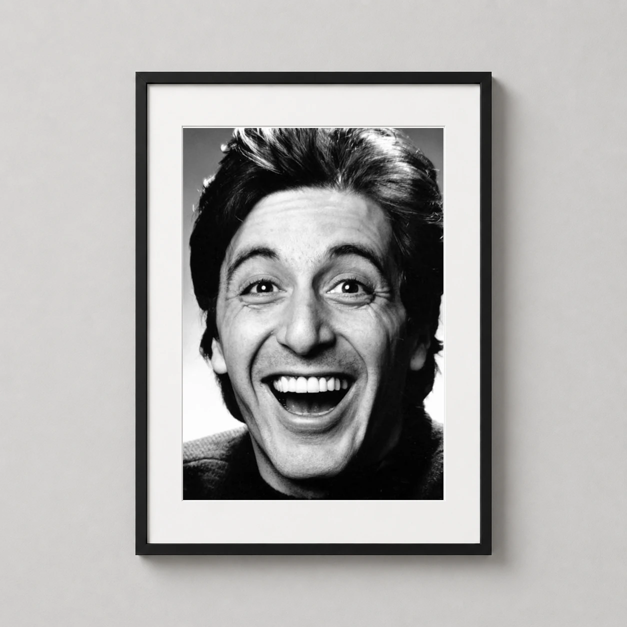 Room mockup of Al Pacino Smiling 1979 Portrait Black and White Photography Print, displayed as framed wall art in a office setting as a portrait print with black and white tones.