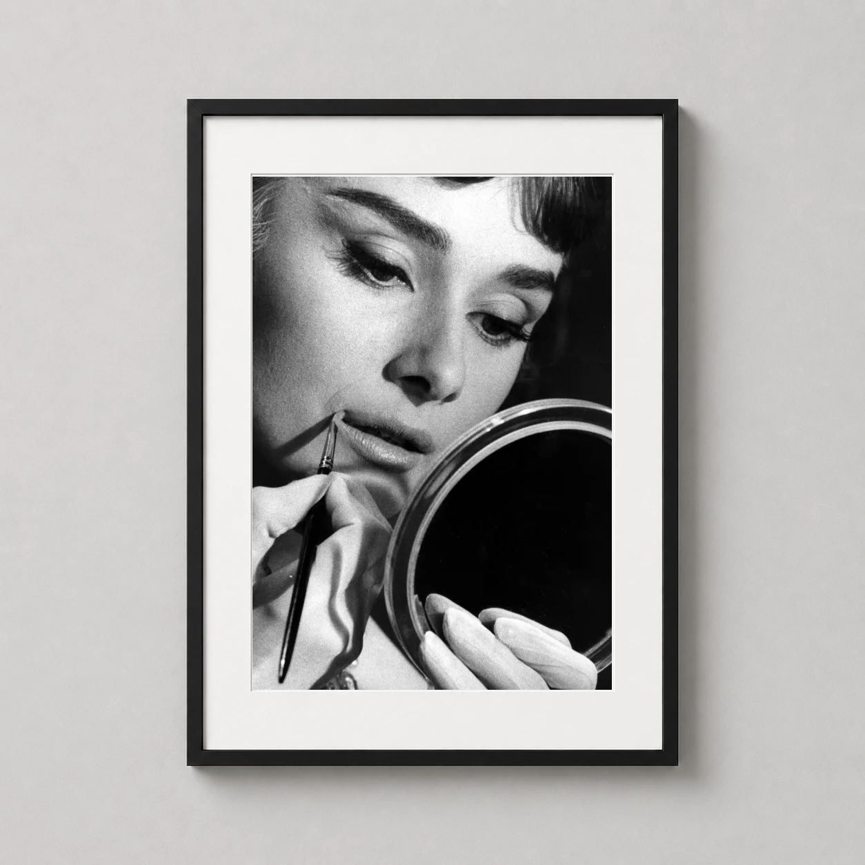 Room mockup of Audrey Hepburn Applying Makeup 1957 Glamour Shot Photography Print, displayed as framed wall art in a home theater setting as a portrait print with black and white tones.