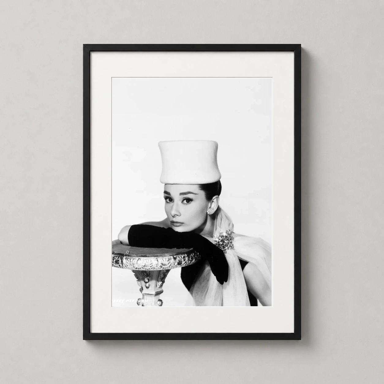 Room mockup of Audrey Hepburn Funny Face Fashion Photography Print, displayed as framed wall art in a office setting as a portrait print with black and white and gold tones.