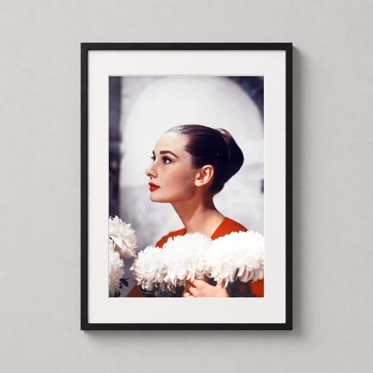 Room mockup of Audrey Hepburn Profile Portrait with White Flowers Movie Poster, displayed as framed wall art in a home theater setting as a portrait print with red and white tones.
