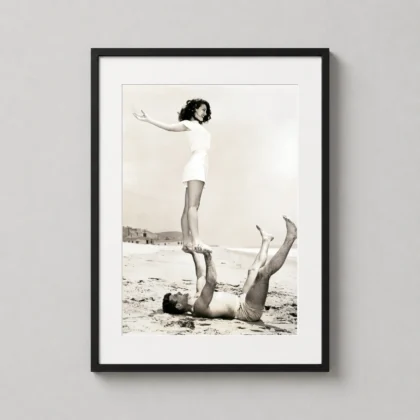 A framed print of Ava Gardner and Burt Lancaster's beach acrobatics hanging in a bright bedroom above a nightstand.