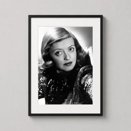 A framed bette davis 1960s art print hanging in a modern living room above a velvet armchair.