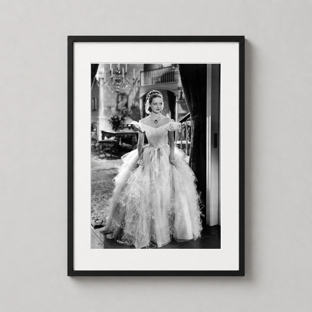 Room mockup of Bette Davis as Julie Marsden in Jezebel, 1938 Movie Photography Print, displayed as framed wall art in a office setting as a portrait print with black and white and gold tones.