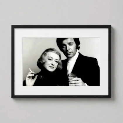 A framed black and white print of Bette Davis and Robert Wagner displayed on a modern office wall above a wooden desk.